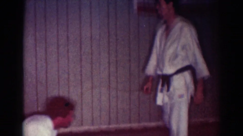 1967 Los Angeles 8mm frame of a karate participant in a white gi and dark belt walking near the mat after the exchange.