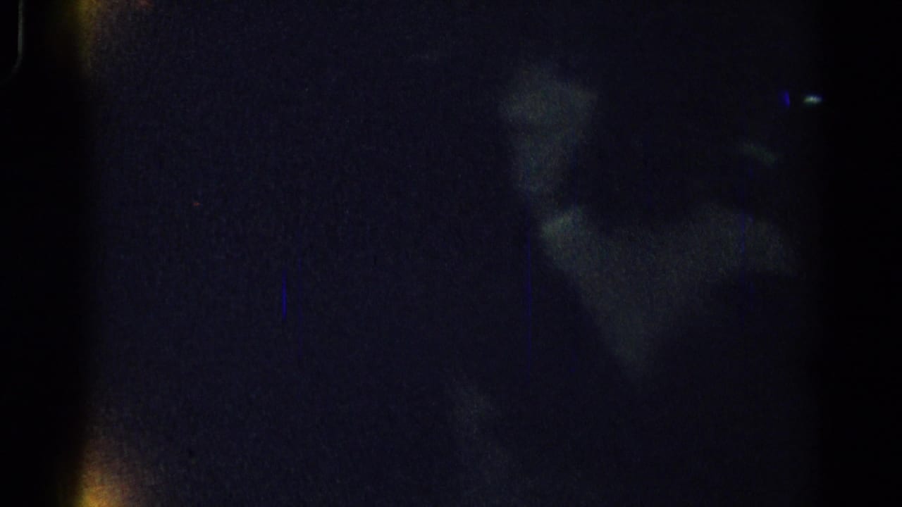 Very dark frame with faint reflections and possible figure shapes.