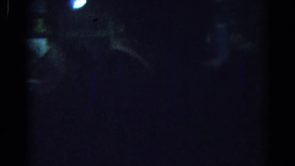 Low-light Los Angeles party frame with a small bright light above and indistinct figures or objects receding into darkness.