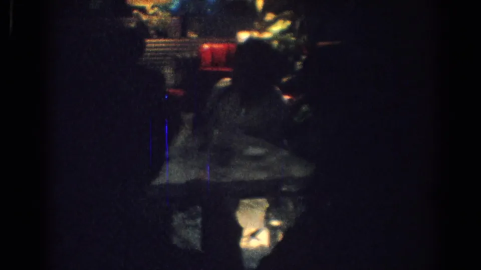 1967 Los Angeles 8mm frame showing a red booth and warm-lit seating area behind a dark foreground figure.