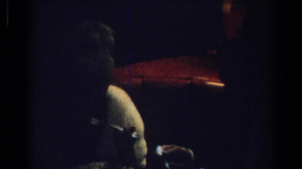 Dim 1967 Los Angeles restaurant footage with a woman in white fur and jewelry seated at a dining table.