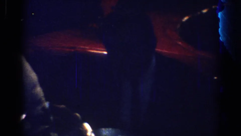 Low-light 1967 Los Angeles 8mm frame showing a seated adult at a dinner table with red ambient lighting behind them.