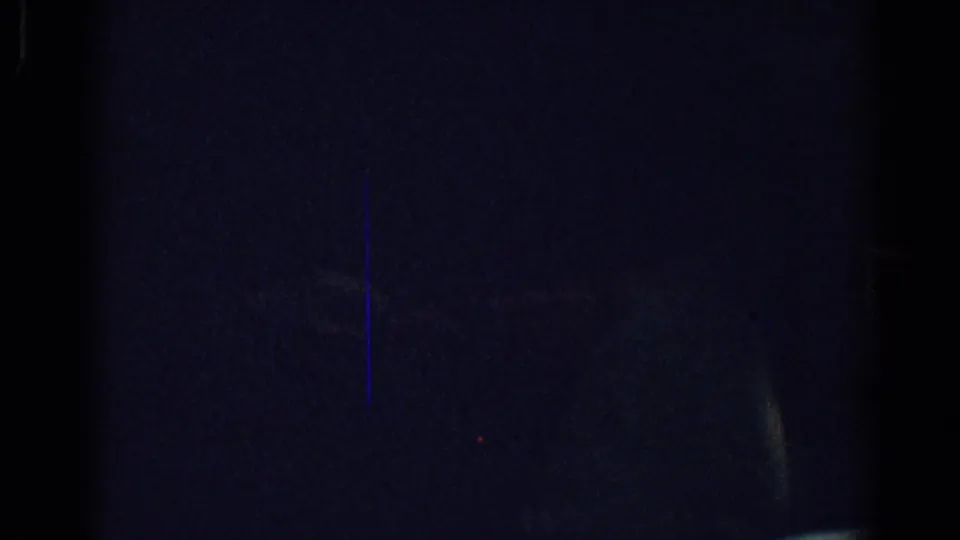 A very dark 1967 Los Angeles dinner frame shows a faint seated figure and a blue vertical flare across the 8mm film image.