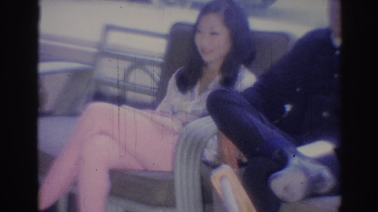 Woman seated on a bench beside a man, with public seating and railing behind them.