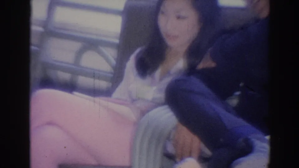 Closer 1967 home-movie frame of the woman and man seated shoulder to shoulder, with the woman's face softly visible.