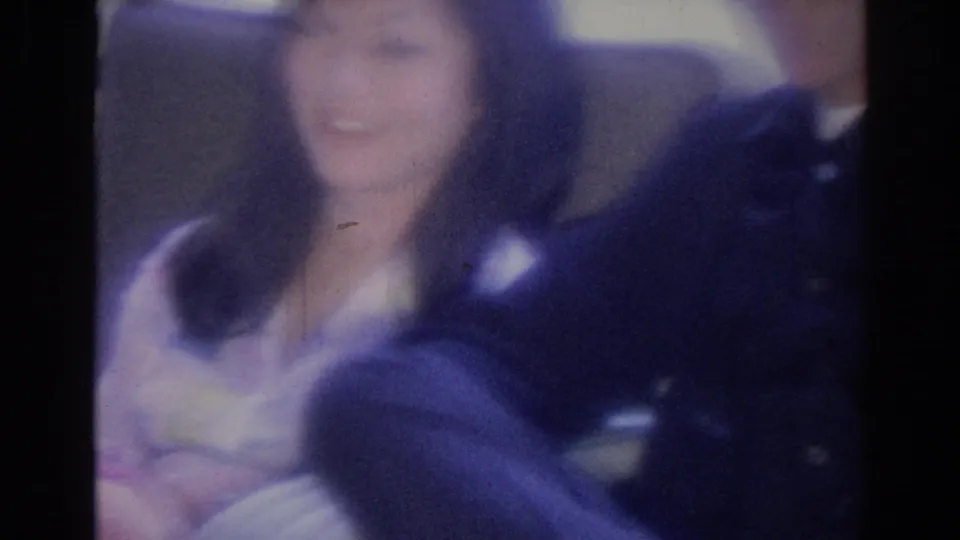 Blurred 8mm frame of the seated woman smiling toward the camera while the man beside her is partly visible.