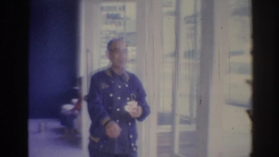 The man holding a mug stands near glass storefront doors, with bright street light visible through the windows.