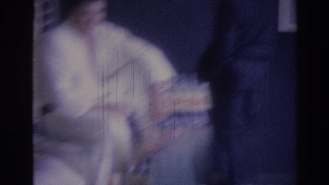 Blurred seated man in a white shirt holding a Pepsi pack indoors.
