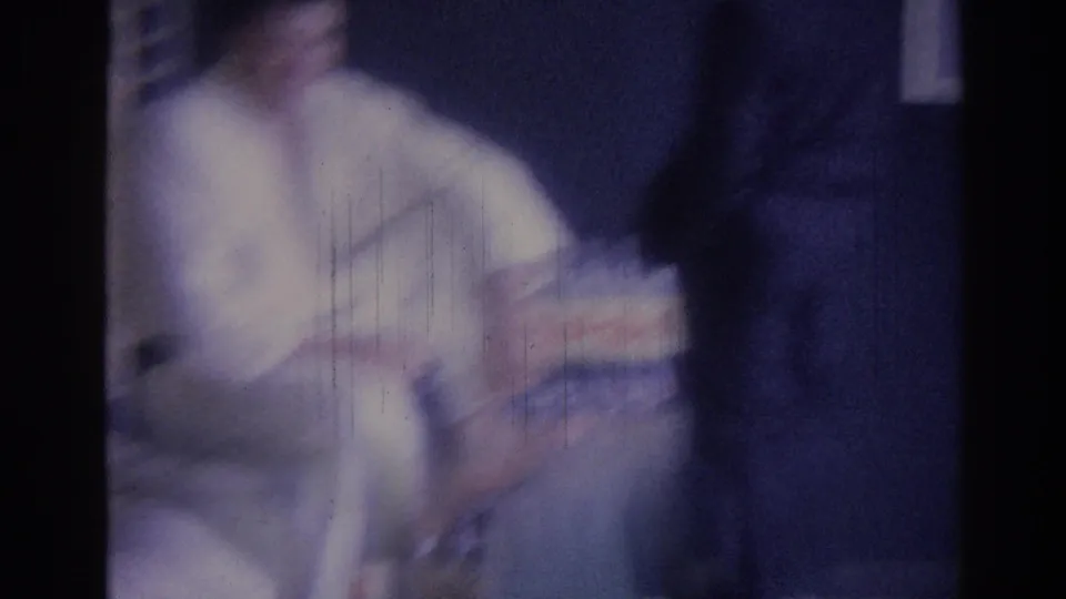 A 1967 Los Angeles home-movie frame shows a blurred seated man in a white shirt holding a Pepsi pack in an interior room.