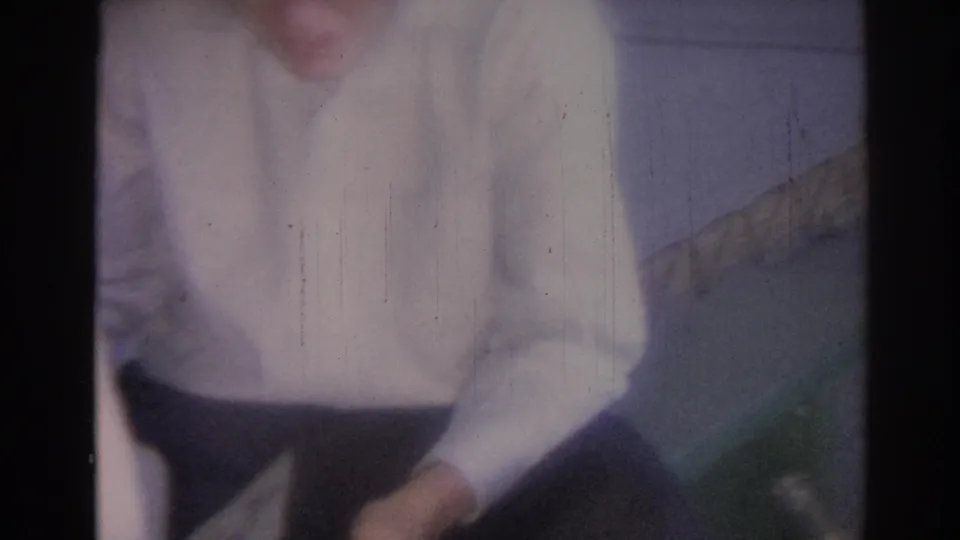 A man in a white shirt and dark pants leans forward in a softly focused 1967 Los Angeles interior home-movie frame.