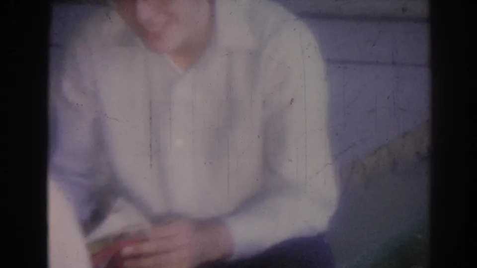 A seated man in a light shirt appears to smile or speak in a faded 1967 Los Angeles 8mm interior frame.