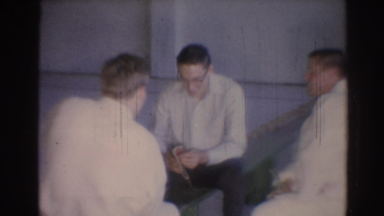 1967 Los Angeles frame of seated men in judo gis, including a man with glasses looking down at a small object.