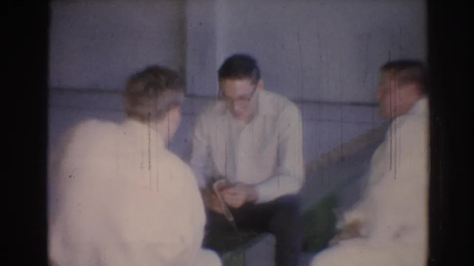 1967 Los Angeles frame of seated men in judo gis, including a man with glasses looking down at a small object.