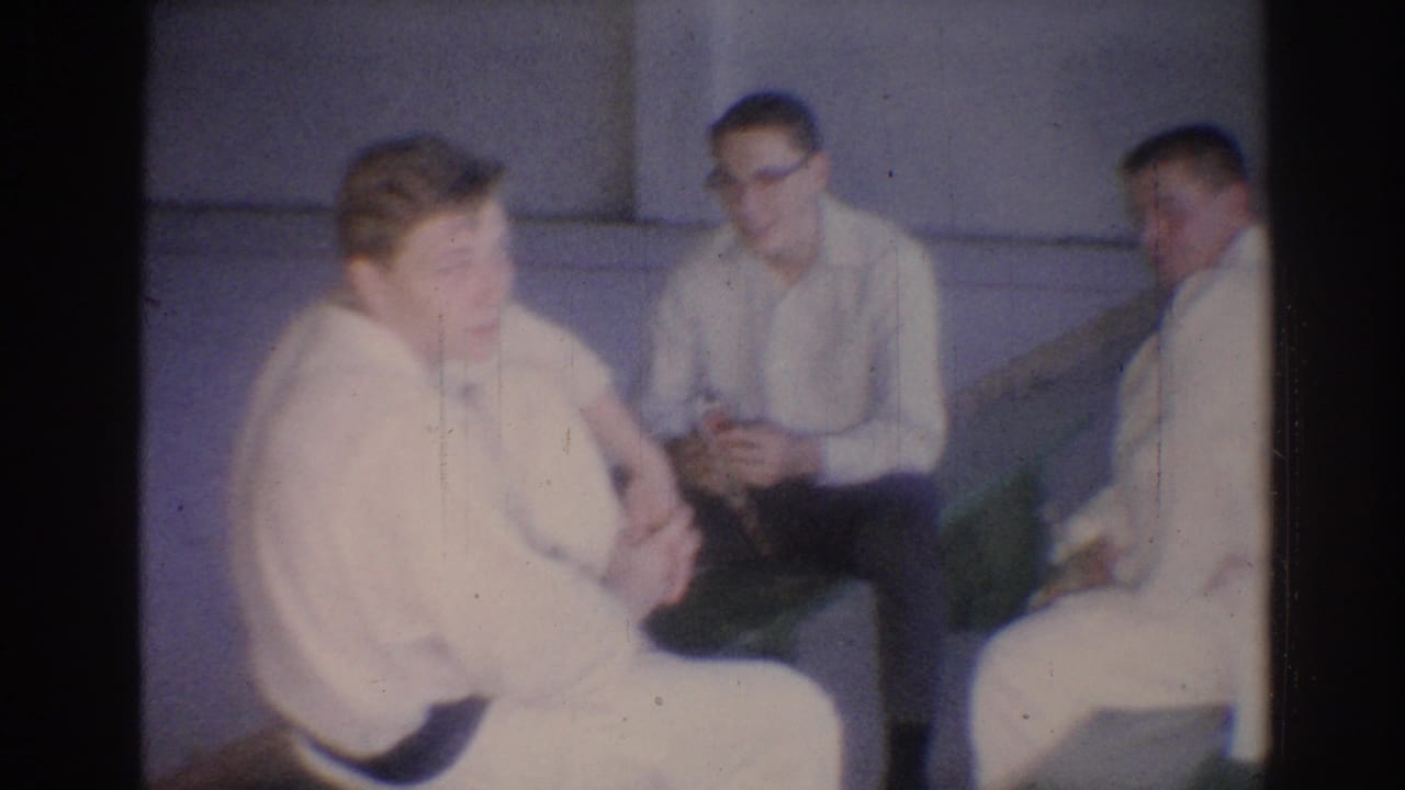 1967 Los Angeles 8mm frame showing several men in white judo gis seated together in an indoor gym.