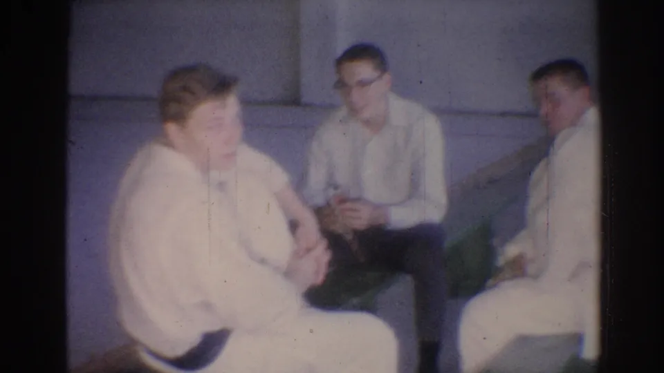 1967 Los Angeles 8mm frame showing several men in white judo gis seated together in an indoor gym.