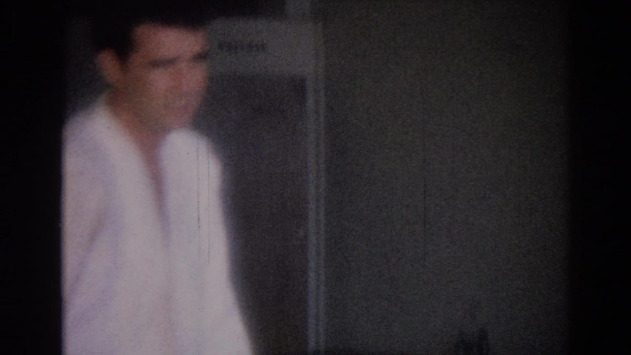 Blurred martial artist in a white gi stands near a wall or doorway.