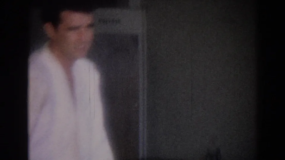 1967 Los Angeles frame with a soft, blurred view of a martial artist in a white gi near an interior wall or doorway.