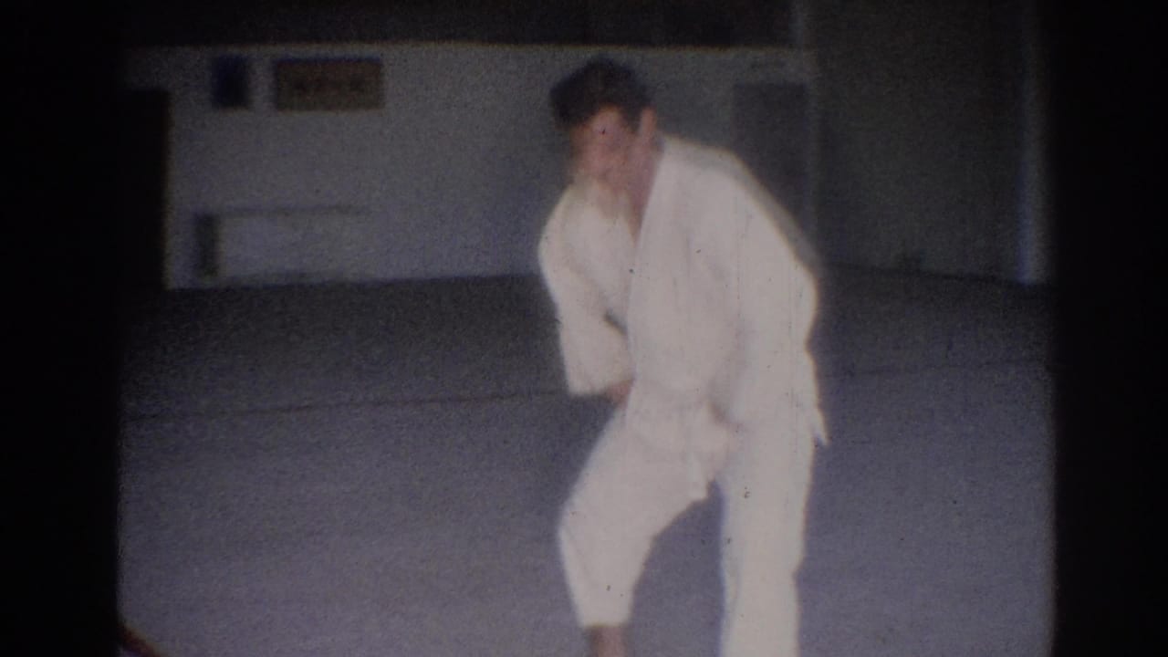 Man in a white judo gi bends into a stance on a pale gym mat.