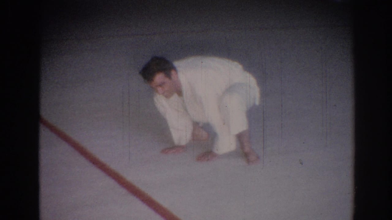 Man in a white gi crouches low beside a red line on the mat.