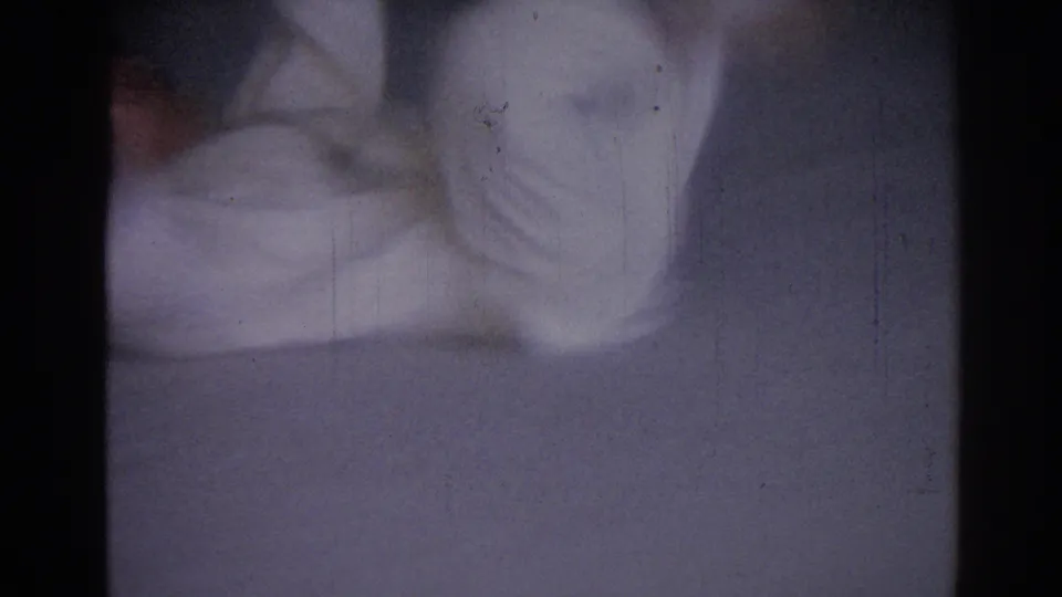 Soft 8mm frame from the Los Angeles judo practice showing a cropped figure in a white gi in motion on the mat.