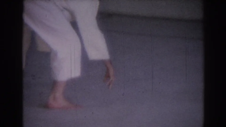 Cropped 1967 Los Angeles judo practice frame showing the athlete's legs and bare feet moving across the indoor mat.