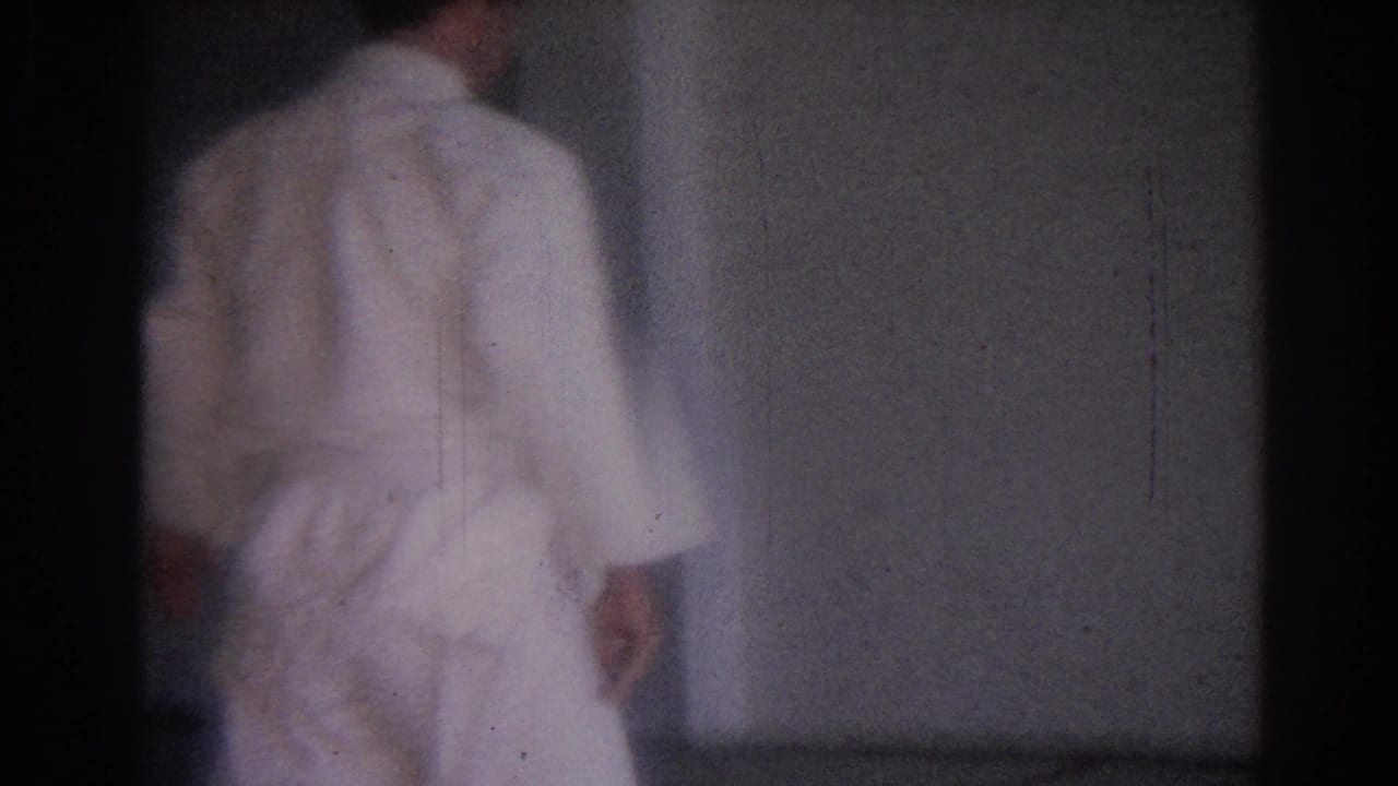 Rear view of a person in a white gi near a plain padded wall.