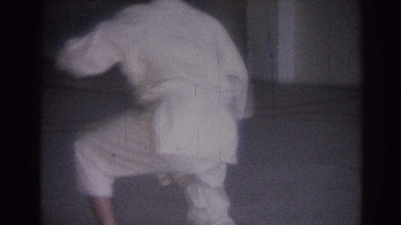 Man in a white martial-arts uniform bends low in a plain indoor room.