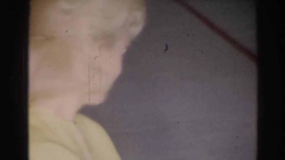 1967 Los Angeles 8mm close frame of the woman in yellow smiling, with plain walls and soft exposure behind her.