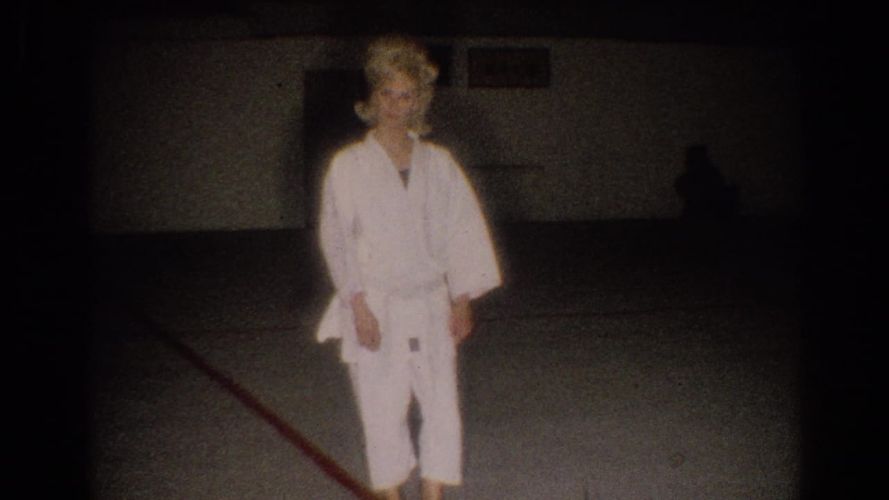Woman in a white karate gi stands in a dim dojo-like room.