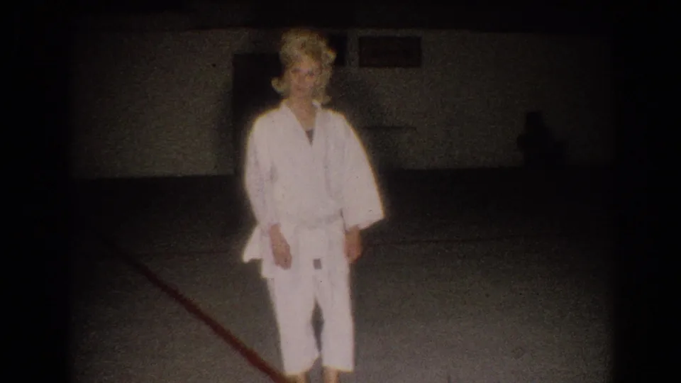 In 1967 Los Angeles home-movie footage, a woman in a white gi faces the camera inside a dim practice room.