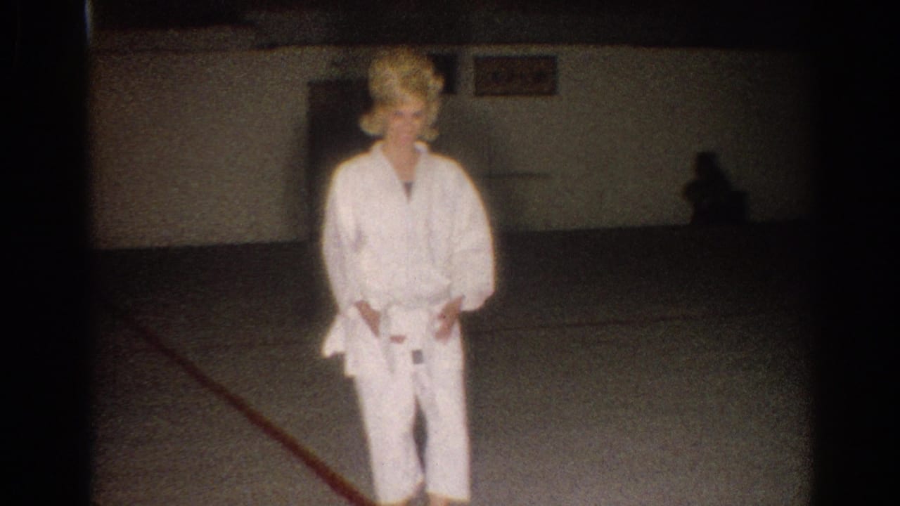 Woman in a white gi looks downward with hands near her belt.