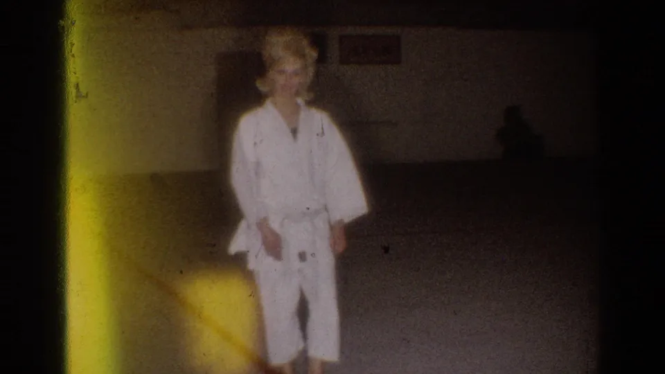 The final frame shows the woman in her gi beside a yellow film flare, with the dim practice room still visible behind her.