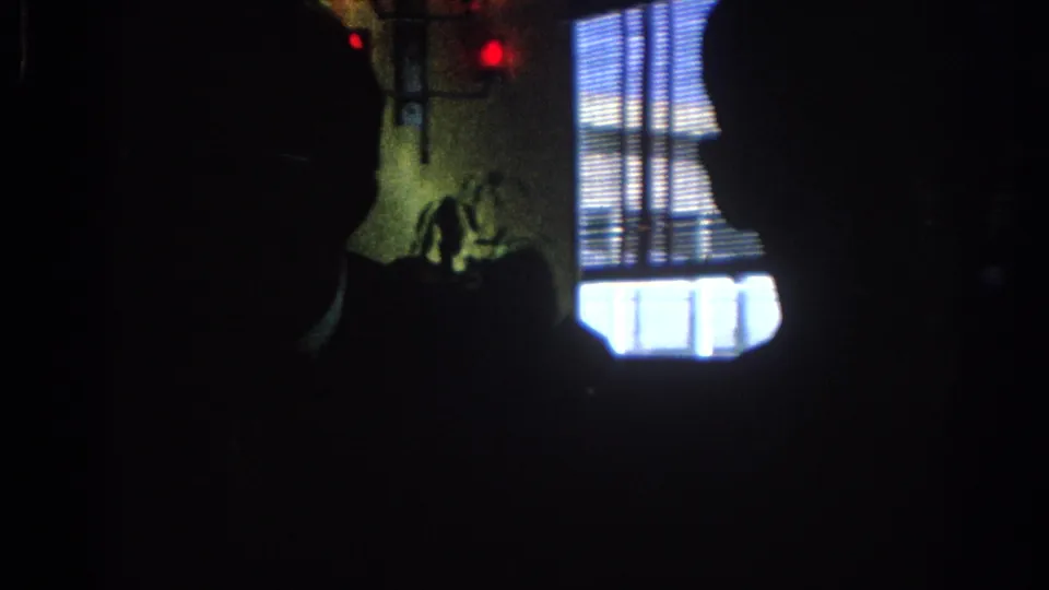 1967 Los Angeles 8mm frame showing silhouetted people in a dark private room beside a bright window with horizontal blinds.