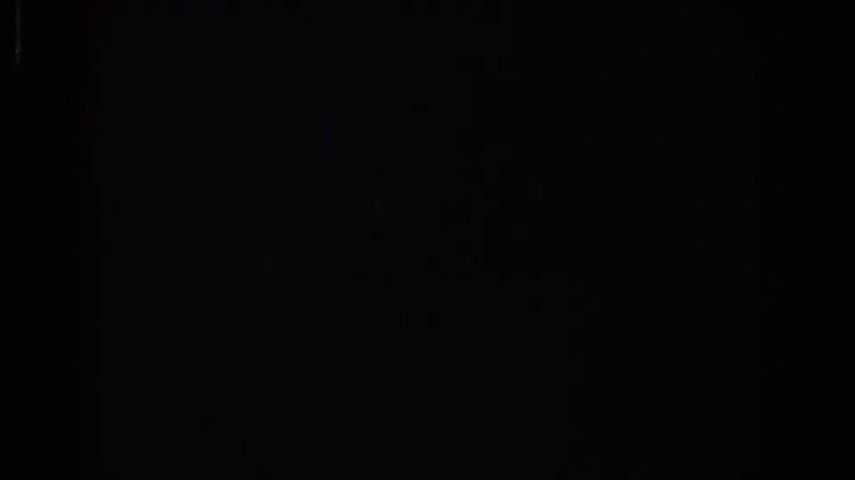 Mostly black 8mm frame within the train footage, showing subtle grain and a faint blue light streak rather than a clear subject.