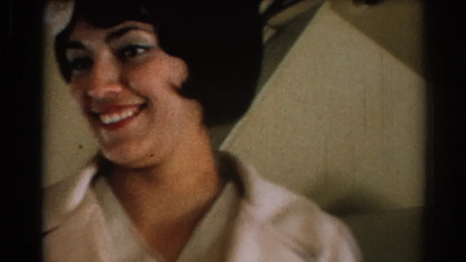 In metadata-supported 1967 footage associated with Los Angeles, a smiling flight attendant with a dark bob hairstyle appears in a light-colored uniform beside aircraft seating.