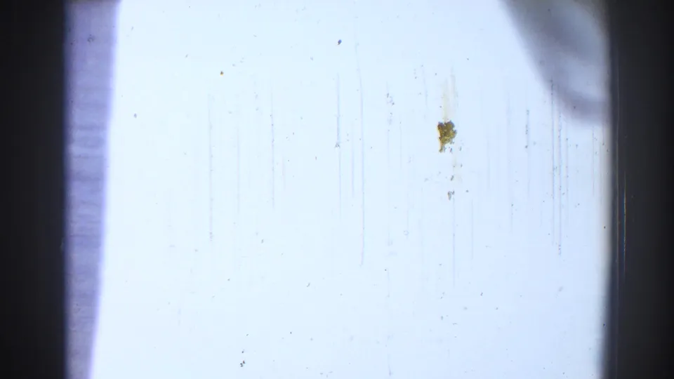 A pale exposed film frame fills the view, showing scratches, dust, vertical marks, and dark 8mm frame edges rather than a clear cabin subject.
