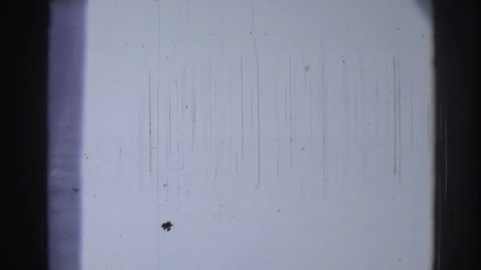 The closing frame shows a pale, scratched 8mm film surface with dust marks, vertical abrasion lines, and a dark border at the edge of the scan.