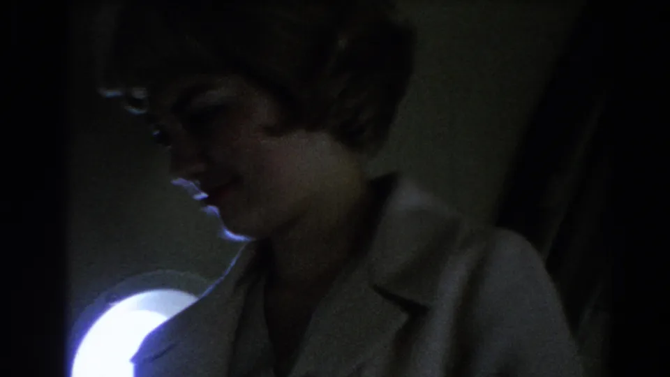 Close passenger-view shot of a stewardess in a light uniform inside a dim 1967 airplane cabin.