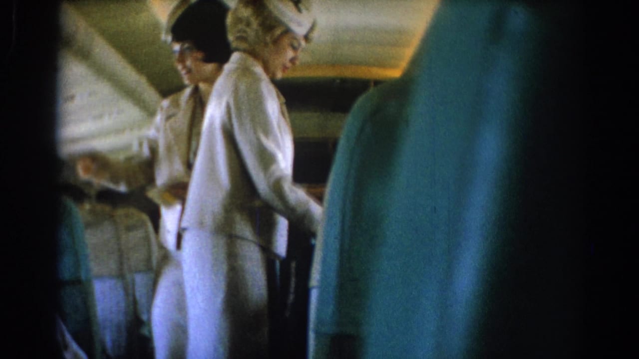 Uniformed attendants stand in the cabin aisle with blue seat backs in the foreground.
