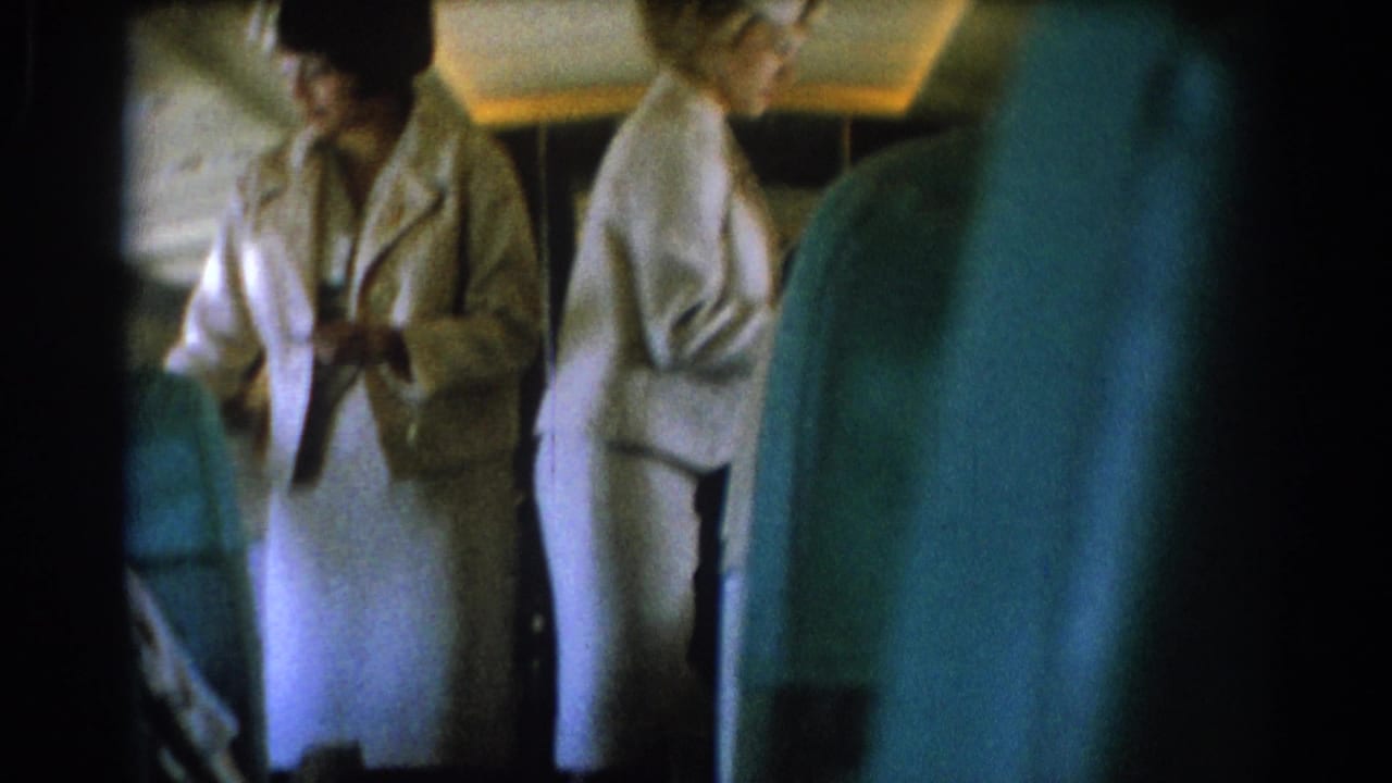 Two flight attendants in white uniforms stand in an airplane aisle near teal-blue seats.