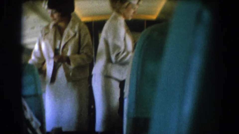 1967 8mm passenger-view footage shows flight attendants in white uniforms moving through a Los Angeles-linked airplane cabin.