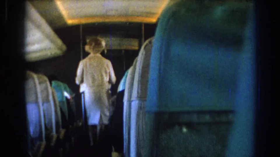 The clip ends on a rear passenger view of a white-uniformed flight attendant moving farther through the 1967 airplane cabin.