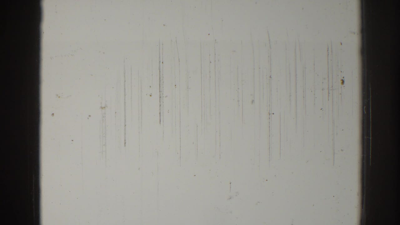 Pale scratched frame with dark vertical borders and dust marks.