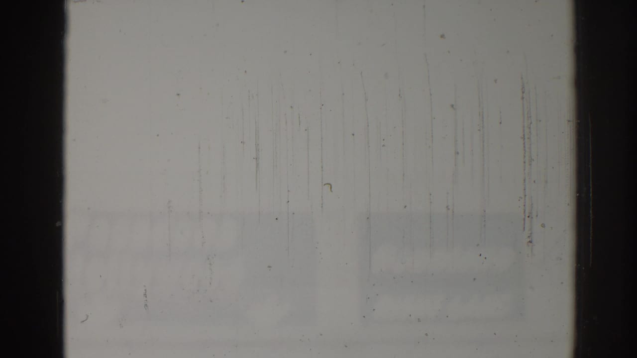 Mostly overexposed film frame with dark borders, scratches, and faint street detail near the lower edge.