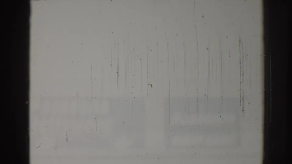 Overexposed 8mm frame from the Los Angeles clip, showing dark film borders, surface scratches, and faint street shapes at the bottom.