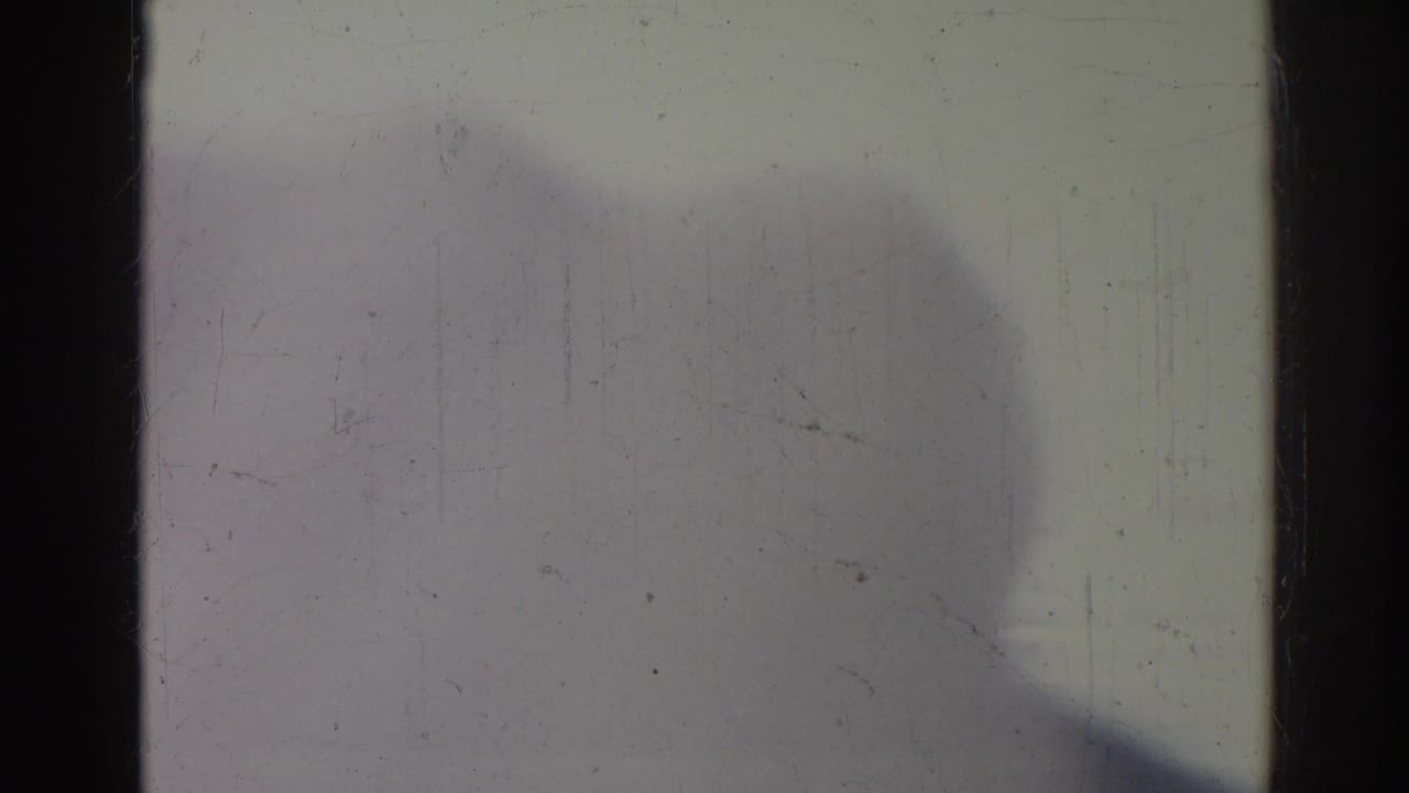 Overexposed frame with a large soft shadow shape, film scratches, and dark vertical borders.