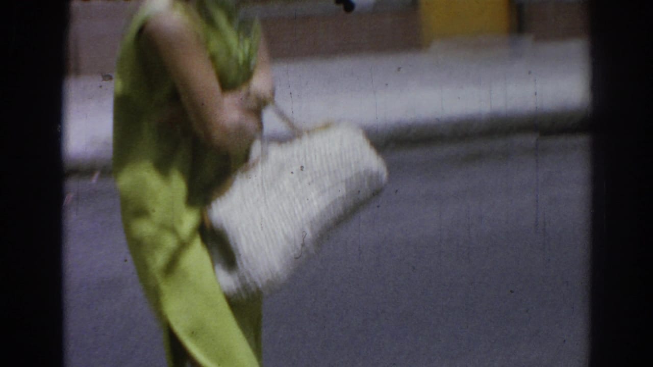 Woman in lime green dress carrying a large white woven purse on a sidewalk.