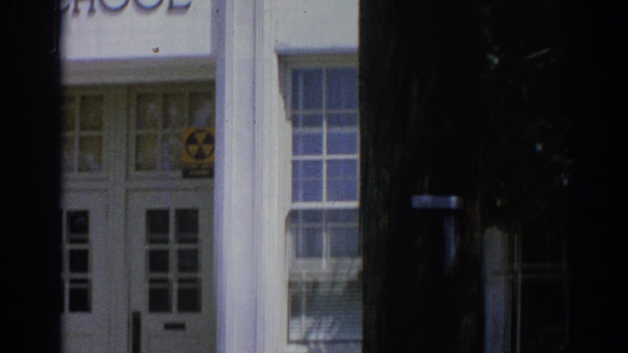 White building entrance with glass doors, columns, steps, and a yellow radiation warning symbol.