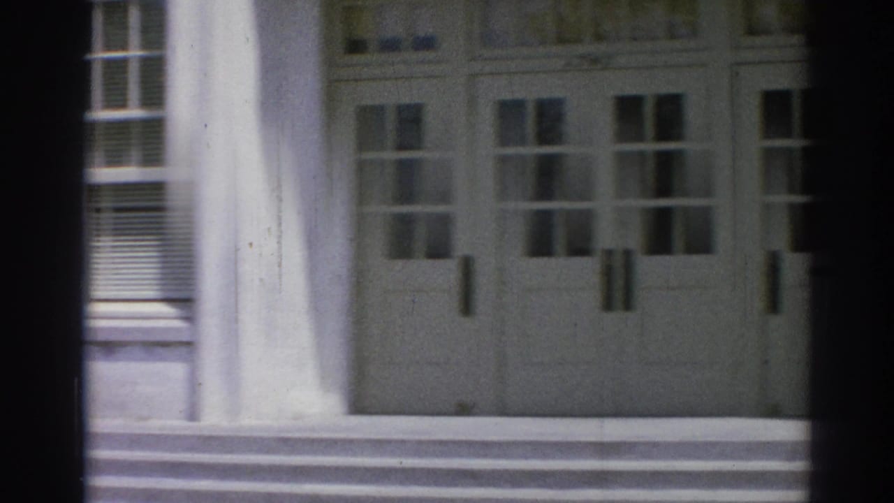 White building facade with double doors, columns, steps, and window panels.