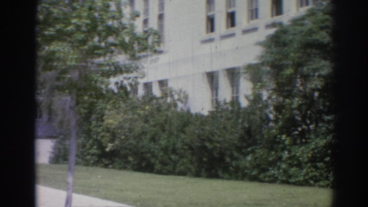 Static 8mm view of a Los Angeles institutional facade with lawn, shrubs, walkway, and dark frame edges.